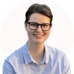 Portrait Olivia, lächelnd, mit Brille, kurzen Haaren und blauem Hemd