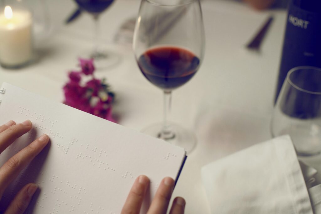 Braille Menü im Vordergrund. Im Hintergrund ein Glas Rotwein auf weißer Tischdecke
